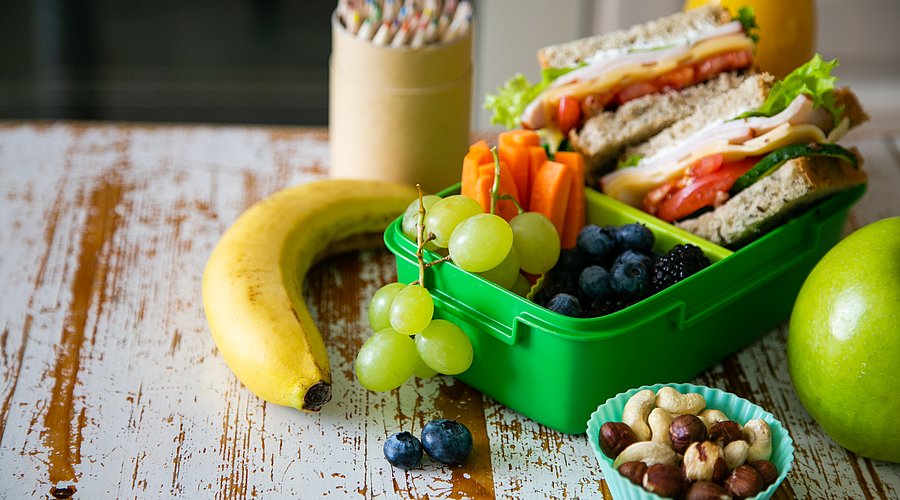 Gefüllte Brotdose mit Butterbroten, Nüssen und Obst steht auf einem Schultisch.