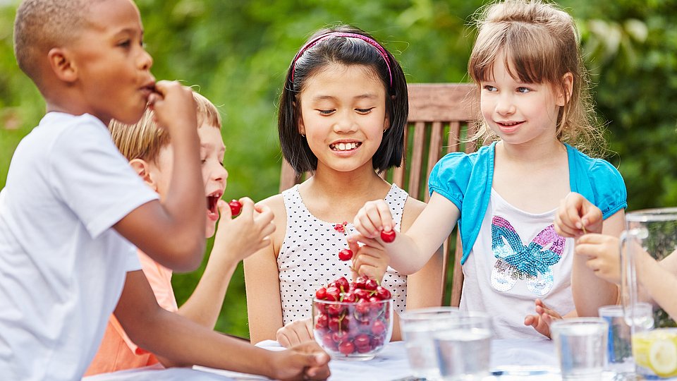 Kinder, die zusammen an einem Tisch sitzen und Kirschen essen.