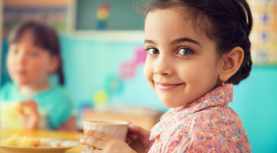 Mädchen in der Kita hält einen Becher und lächelt in die Kamera