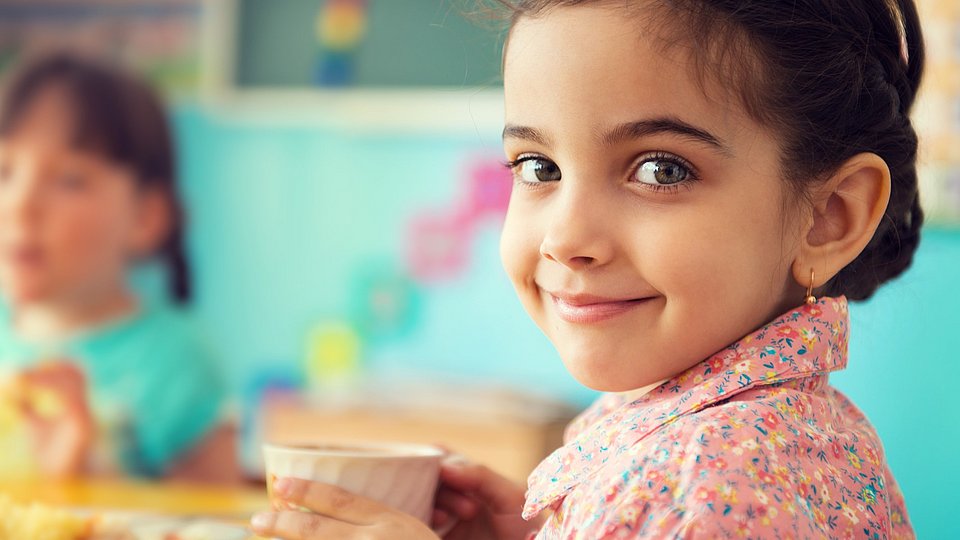 Mädchen in der Kita hält einen Becher und lächelt in die Kamera