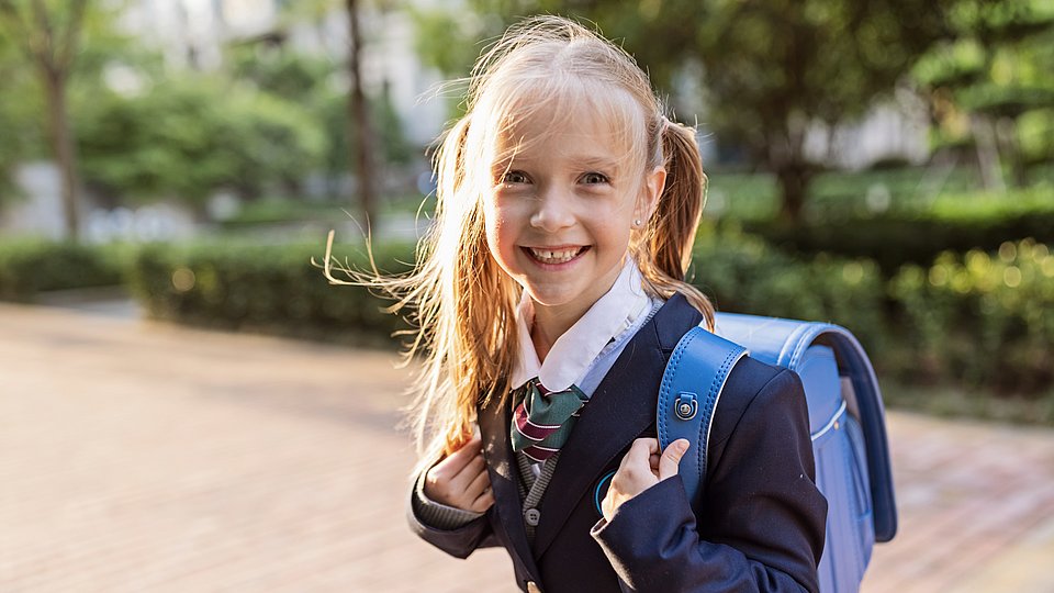 Britisches Grundschulmädchen in Schuluniform und Tornister.