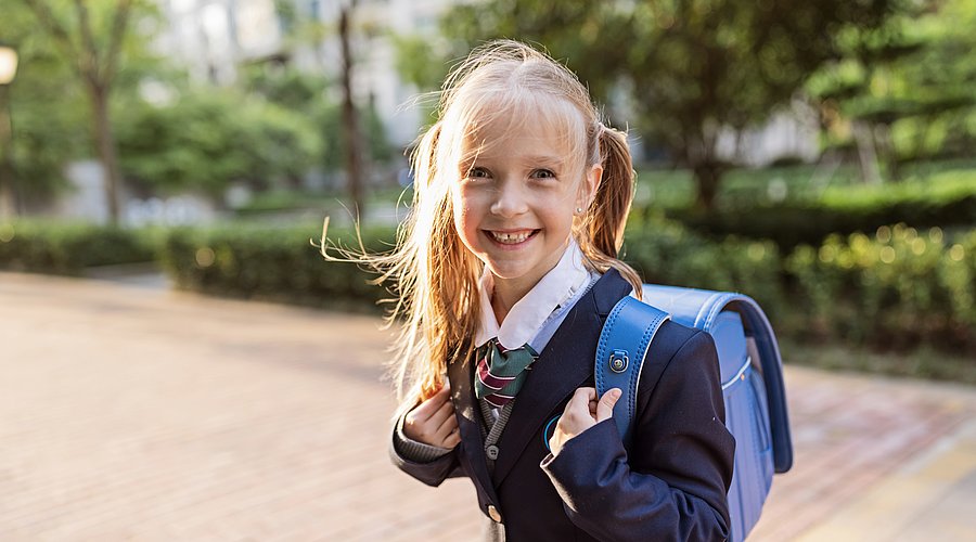 Britisches Grundschulmädchen in Schuluniform und Tornister.