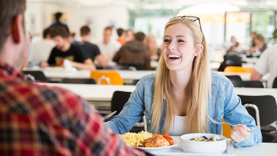 Zwei ältere Schüler sitzen gut gelaunt in der Mensa und essen Mittag 