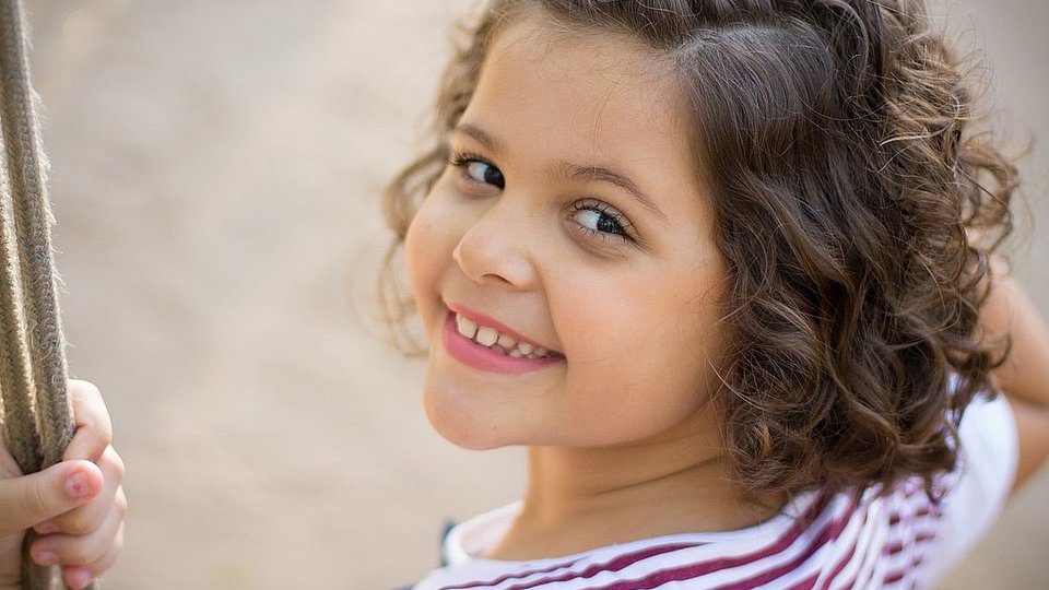 Ein Mädchen im Kindergartenalter sitzt auf einer Schaukel und schaut über ihre Schulter.