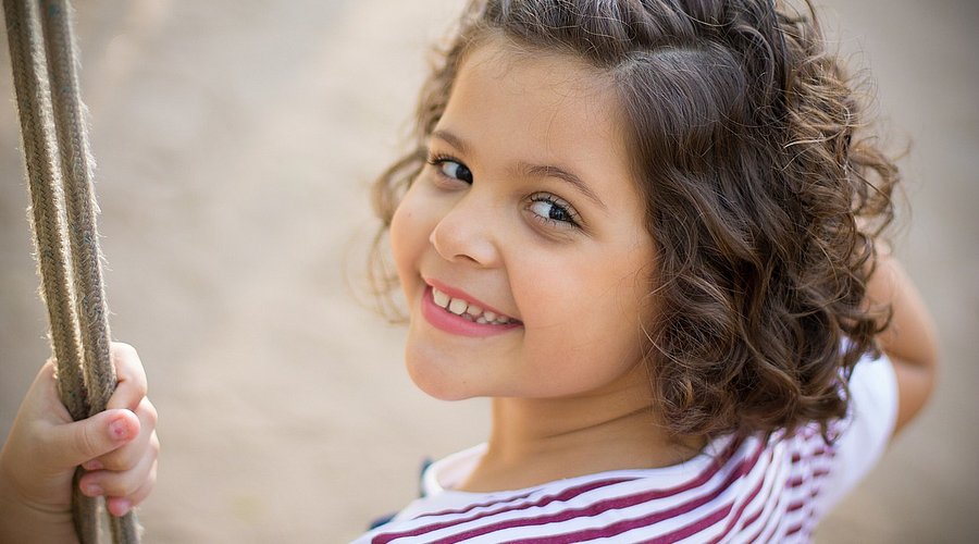 Ein Mädchen im Kindergartenalter sitzt auf einer Schaukel und schaut über ihre Schulter.