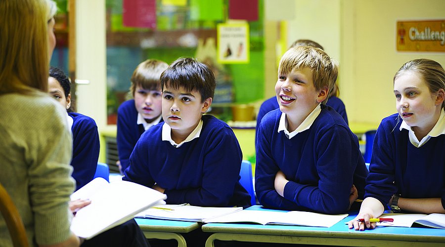 Kinder in Schuluniform sitzen in einer Schulklasse und hören ihrer Lehrerin zu.