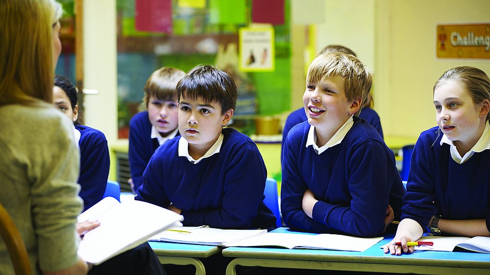 Kinder in Schuluniform sitzen in einer Schulklasse und hören ihrer Lehrerin zu.