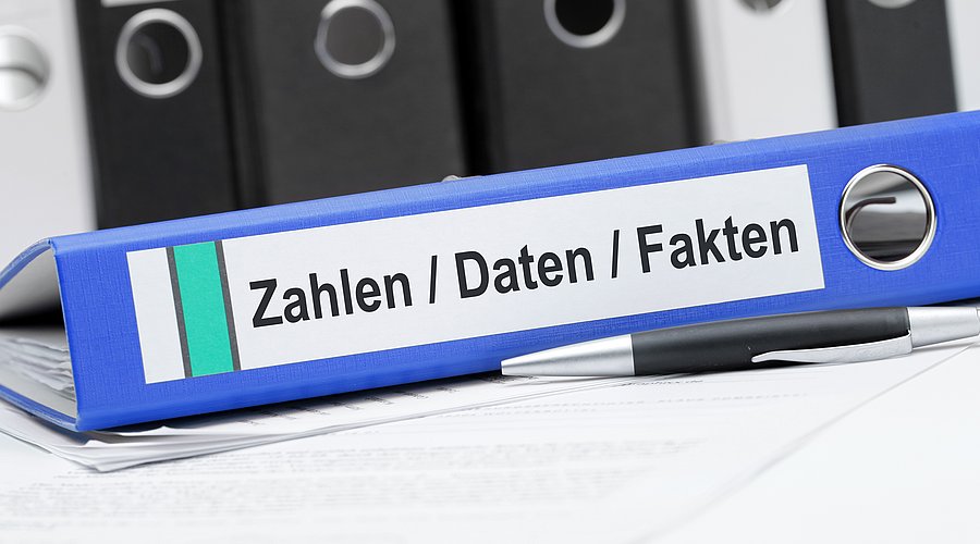 Blauer Ordner zu Zahlen, Daten, Fakten liegt auf dem Tisch