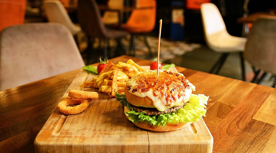 Auf einem Holzbrettchen liegt ein Burger mit Pommes frites.