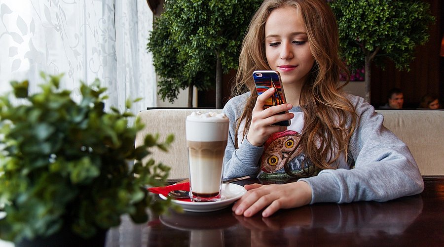 Jugendliche trinkt Latte Macciato und liest in ihrem Handy.