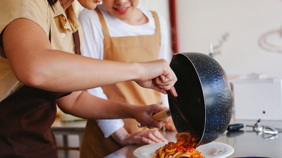 Jugendliche Schülerinnen bereiten sich Spaghetti mit Tomatensauce zu. 