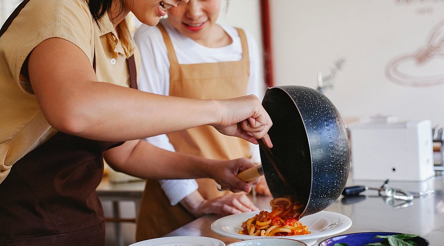 Jugendliche Schülerinnen bereiten sich Spaghetti mit Tomatensauce zu. 