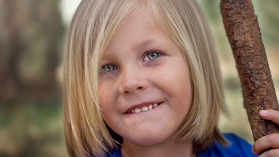 Junge mit schulterlangen blonden Haaren lächelt in die Kamera.