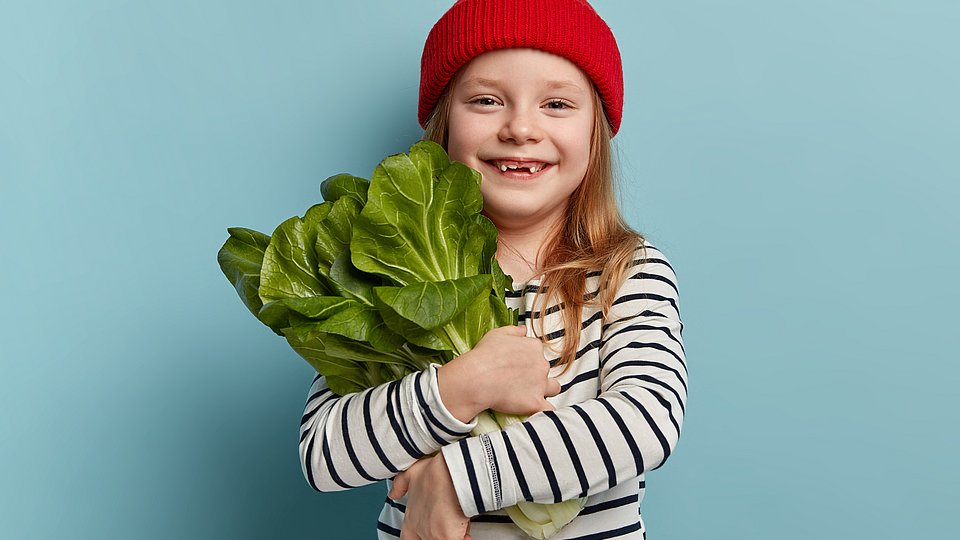 Kita-Kind hält Pak-Choi im Arm und lacht. 