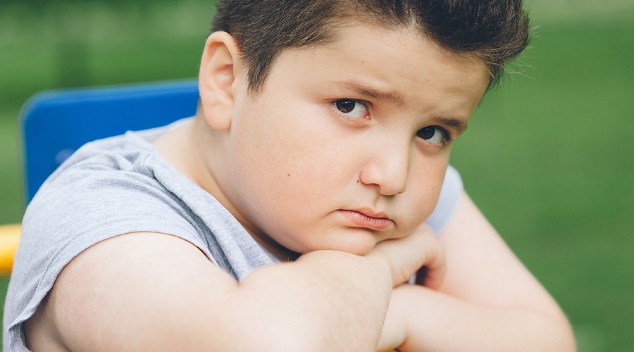 Ein etwas übergewichtiger Junge hat den Kopf auf seine Hände gestützt und schaut traurig in die Kamera. 