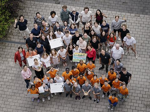 Alle beim Schulwettbewerb Echt kuh-l im Jahr 2023 ausgezeichneten Schülerinnen und Schüler, die auf einem Schulhof stehen und nach oben schauen. Das Bild ist aus der Vogelperspektive gemacht. 