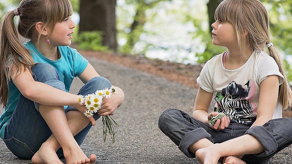 Zwei junge Mädchen sitzen auf der Straße und unterhalten sich.