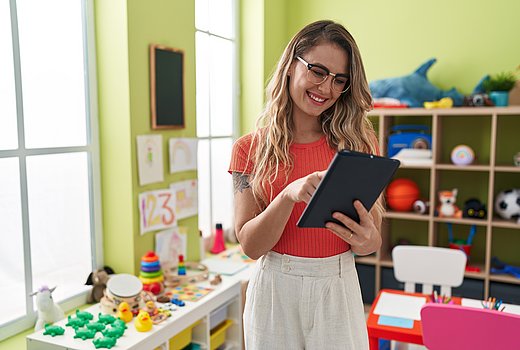 Eine junge Frau mit auffallender Brille, langen blonden Haaren und einem Arm-Tattoo hält ein elektronisches Tablet in der Hand und tippt auf den Bildschirm. Sie lacht.