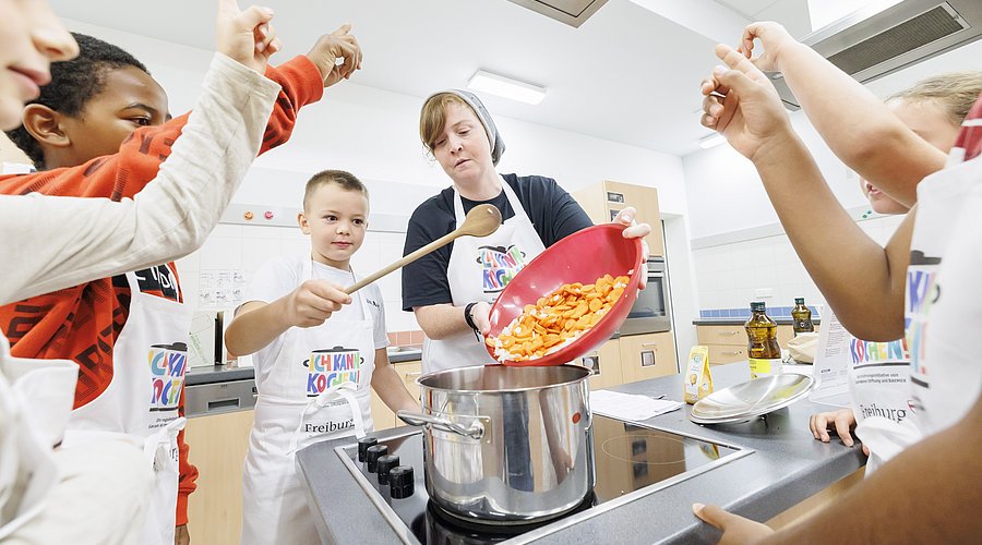 Kinder kochen gemeinsam mit einer Fachkraft in der Küche einen Eintopf. 