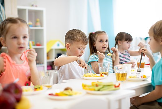 Kitakinder sitzen am Tisch und essen gemeinsam Mittag 