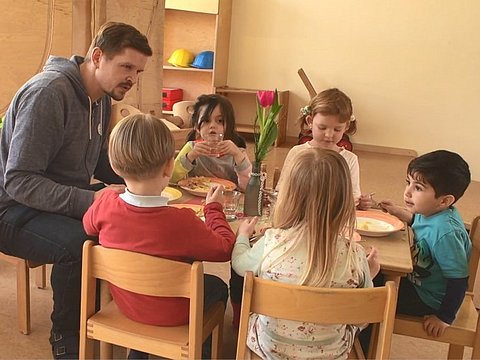 Erzieher sitzt gemeinsam mit Kindern am Mittagstisch.