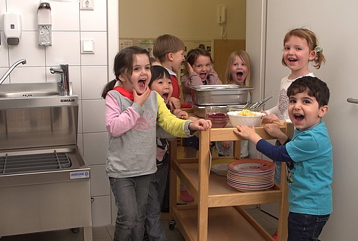 Kita-Kinder bringen schmutziges Geschirr nach dem Essen in die Küche.