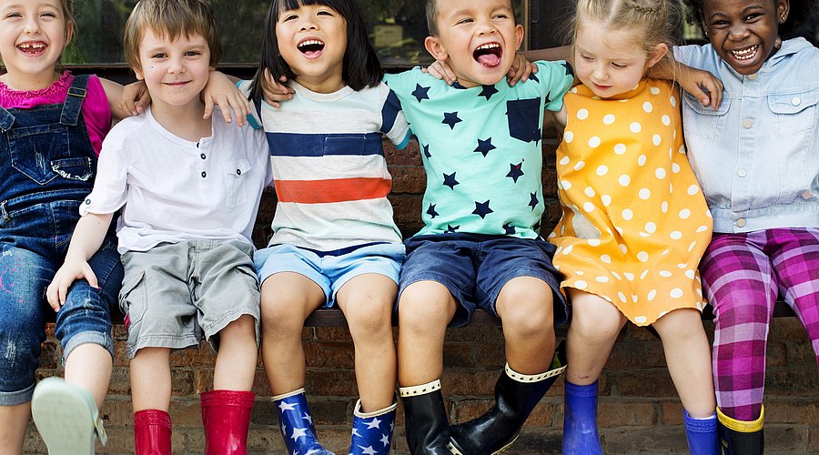 Kindergartenkinder sitzen nebeneinander auf einer Mauer und lachen