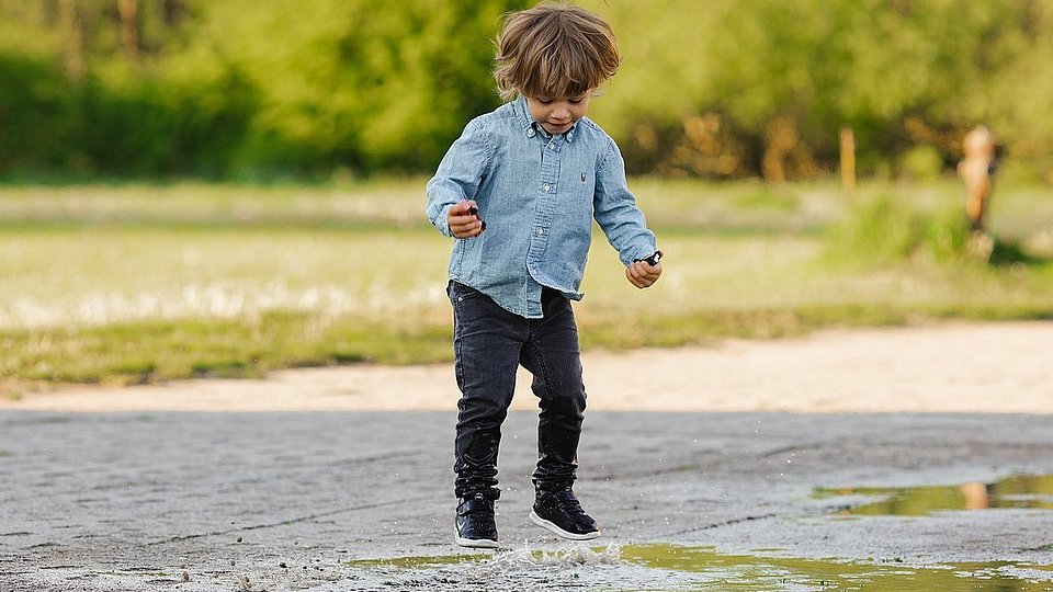 Ein Junge im Kindergartenalter springt in einer Pfütze auf und ab.