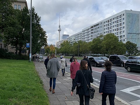 Veranstaltungsteilnehmende im Gespräch auf dem Gehweg an einer Straße