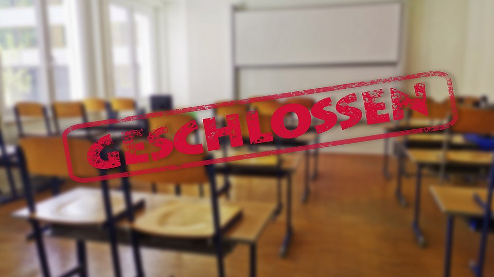 In einem Klassenzimmer sind alle Stühle hochgestellt. Quer über das Bild verläuft ein Banner mit dem Wort "Geschlossen". 