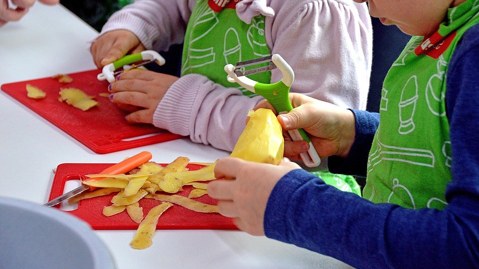 Kinder in Kochschürzen schälen Kartoffeln