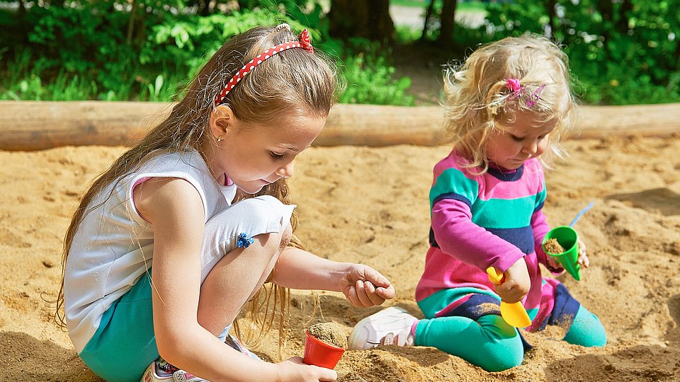 Ein Junge und ein Mädchem im Kita-Alter spielen in einem Sandkasten.