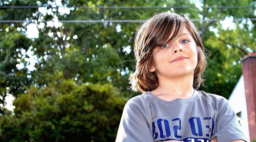 Ein Junge im Teenageralter steht mit verschränkten Armen in einem Garten. 