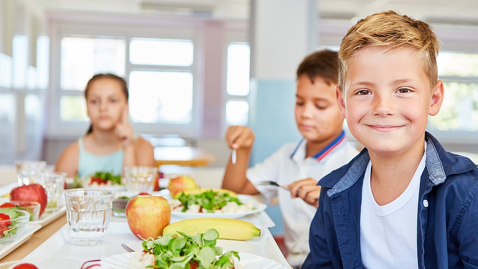 Schüler*innen sitzen in der Mensa an gefüllten Tellern.