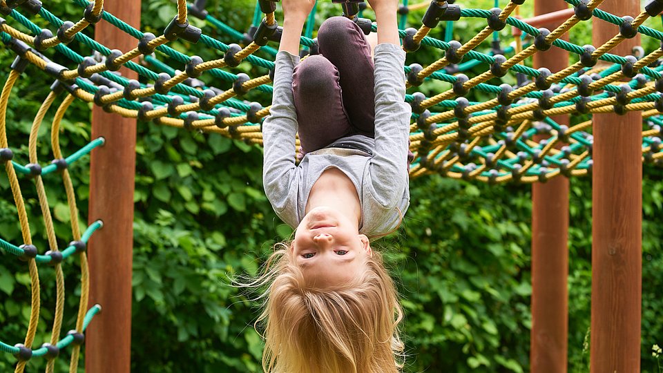 Ein Kita-Kind hängt kopfüber an einem Spielgerät.