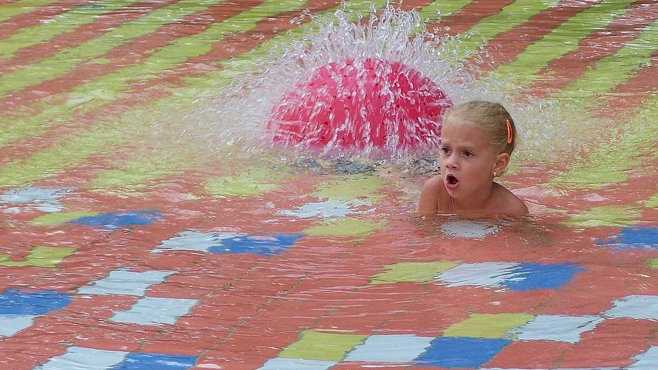 Kleines Mädchen sitzt in einem Kinderschwimmbad mit Wasserfontäne. 