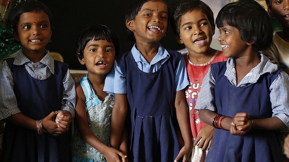 Indische Grundschulkinder stehen in Schuluniform in einer Gruppe zusammen und lachen.