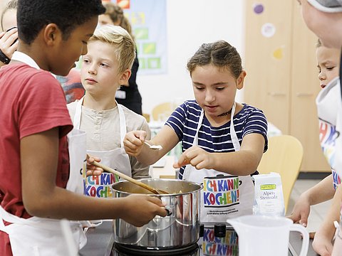 Kinder rühren zusammen in einem großen Topf. 