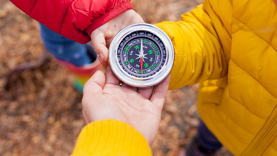 Drei Kinderhände halten zusammen einen Kompass.