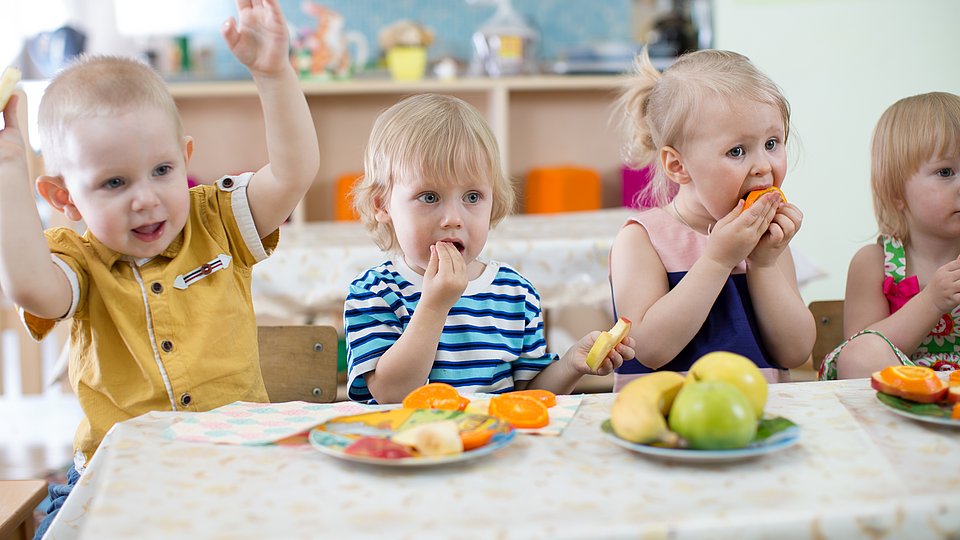 Kitakinder essen gemeinsam an einem Tisch 