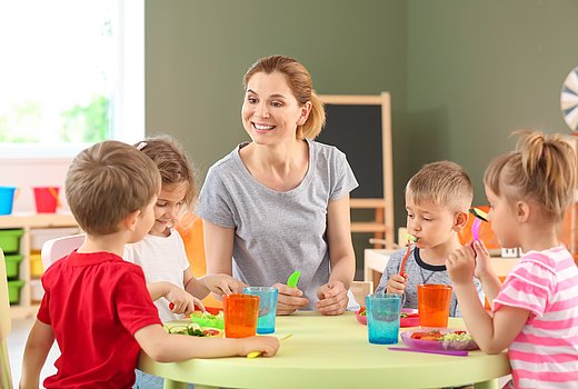 Kinder sitzen um einen Tisch mit buntem Geschirr