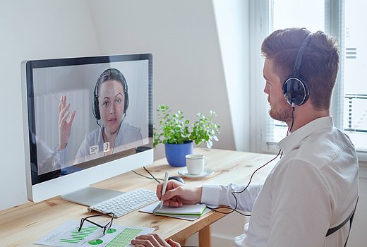 Mann sitzt am Schreibtisch im Büro und nimmt an einem Webseminar teil.