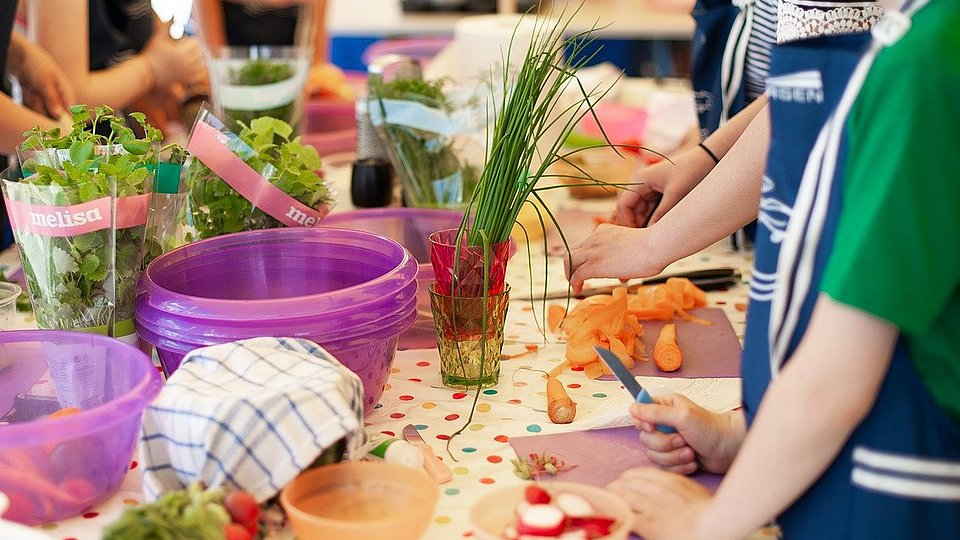 Schulkinder stehen an einem Tisch und schneiden Gemüse.