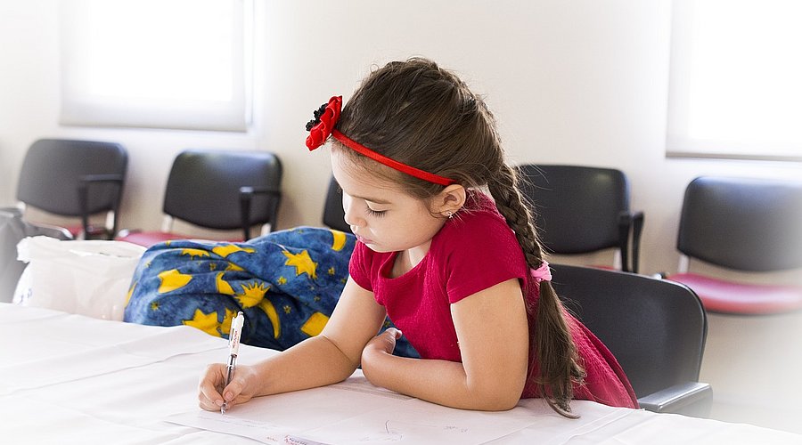 Schulmädchen sitzt am Tisch und schreibt in ein Schulheft. 