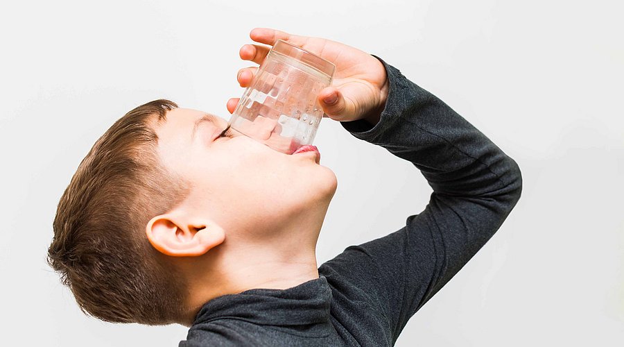 Junge der ein Glas Wasser leer trinkt 