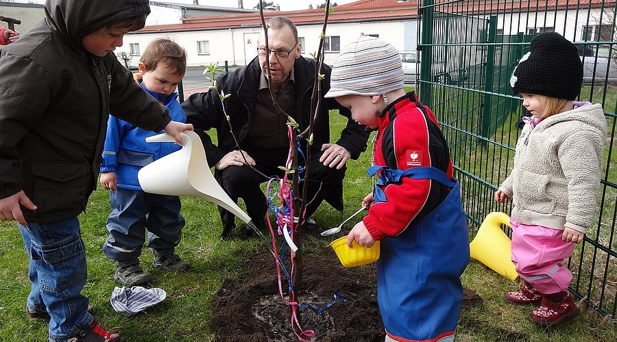 Kindergartenkinder pflanzen gemeinsam mit einem Erzieher einen Baum